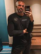 Person taking a mirror selfie wearing a black jacket with a logo.